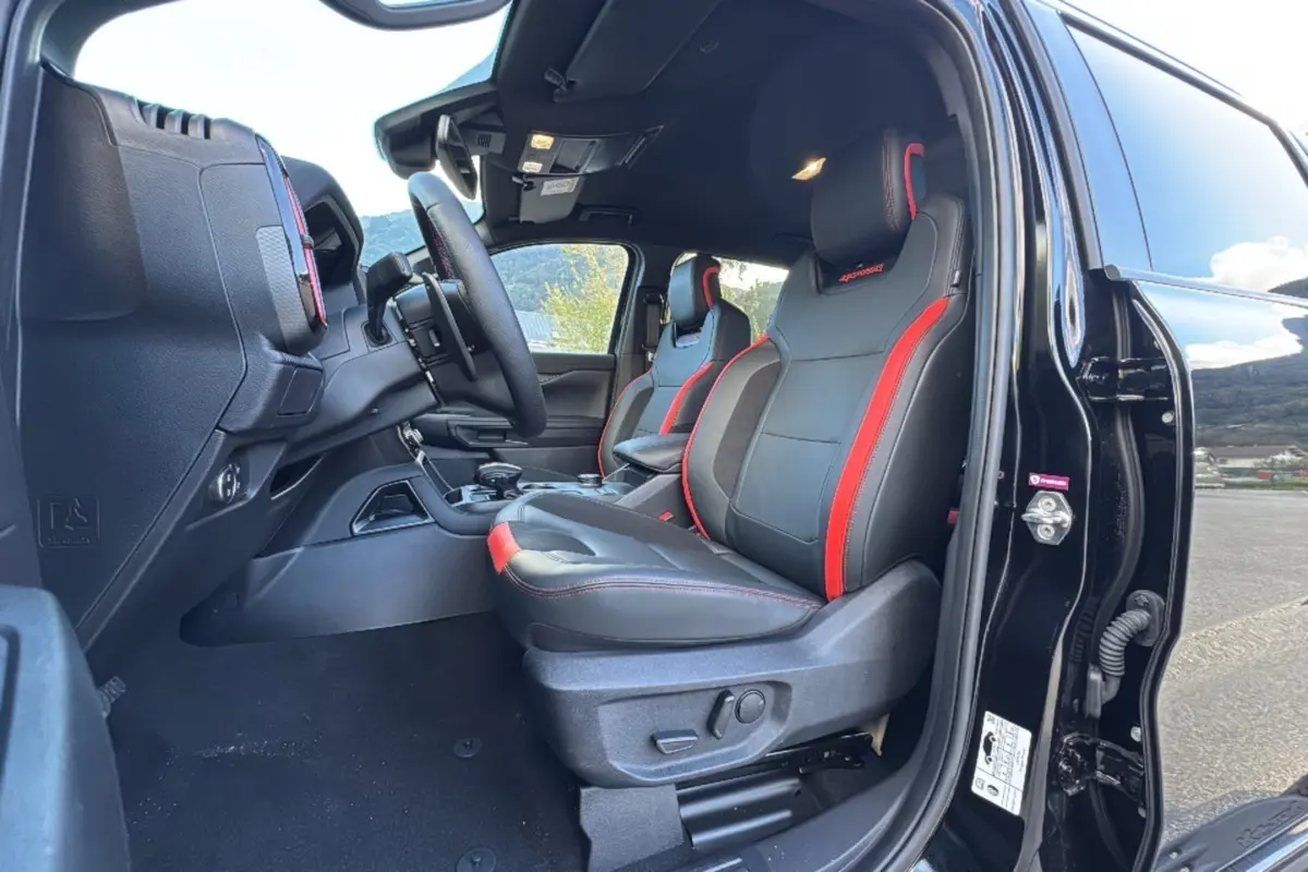 Vue intérieure côté conducteur du Ford Ranger Raptor 2024 noir absolu, sièges sport noirs avec surpiqûres rouges.