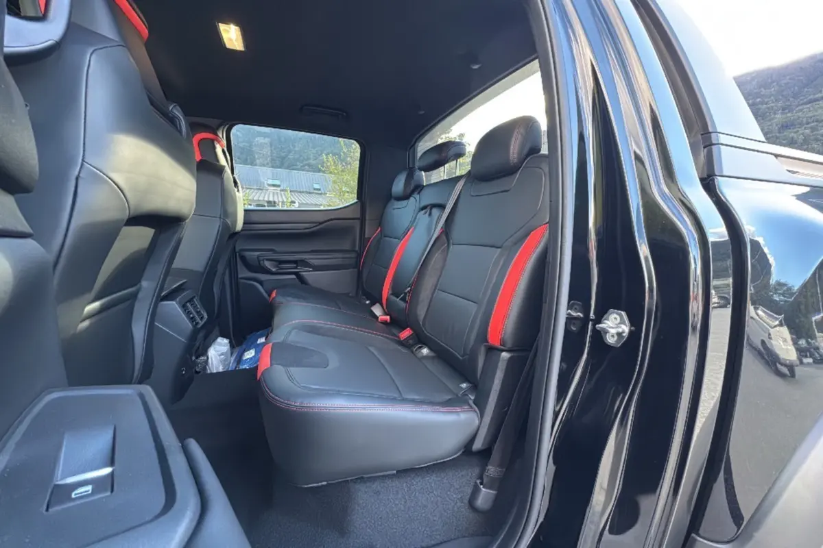Vue intérieure côté droit arrière du Ford Ranger Raptor 2024 noir absolu, sièges en cuir noir avec surpiqûres rouges.