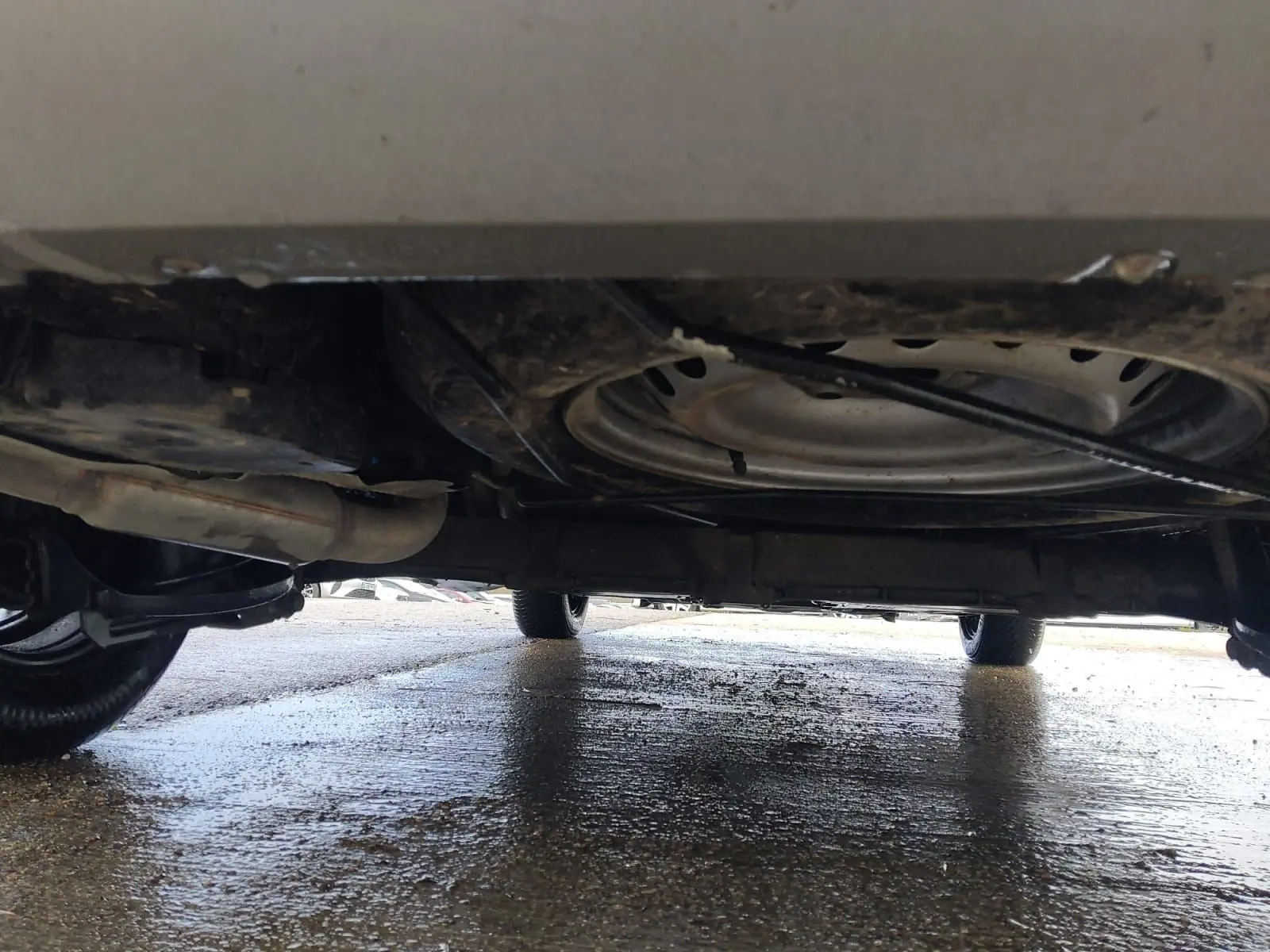 Vue sous le Renault Kangoo blanc 2022, montrant la roue de secours et le châssis sur sol humide.