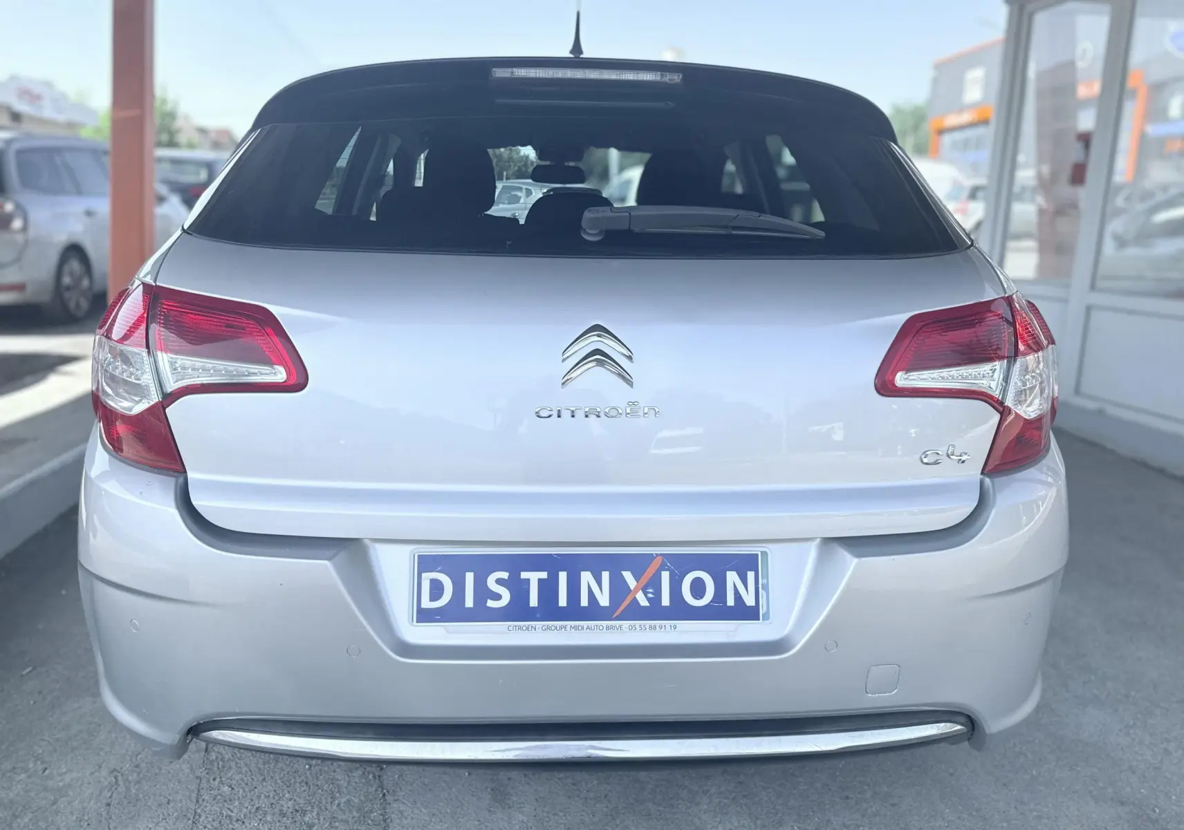 Vue arrière d'une Citroën C4 gris clair, mettant en valeur les feux arrière et le logo central sur un parking.