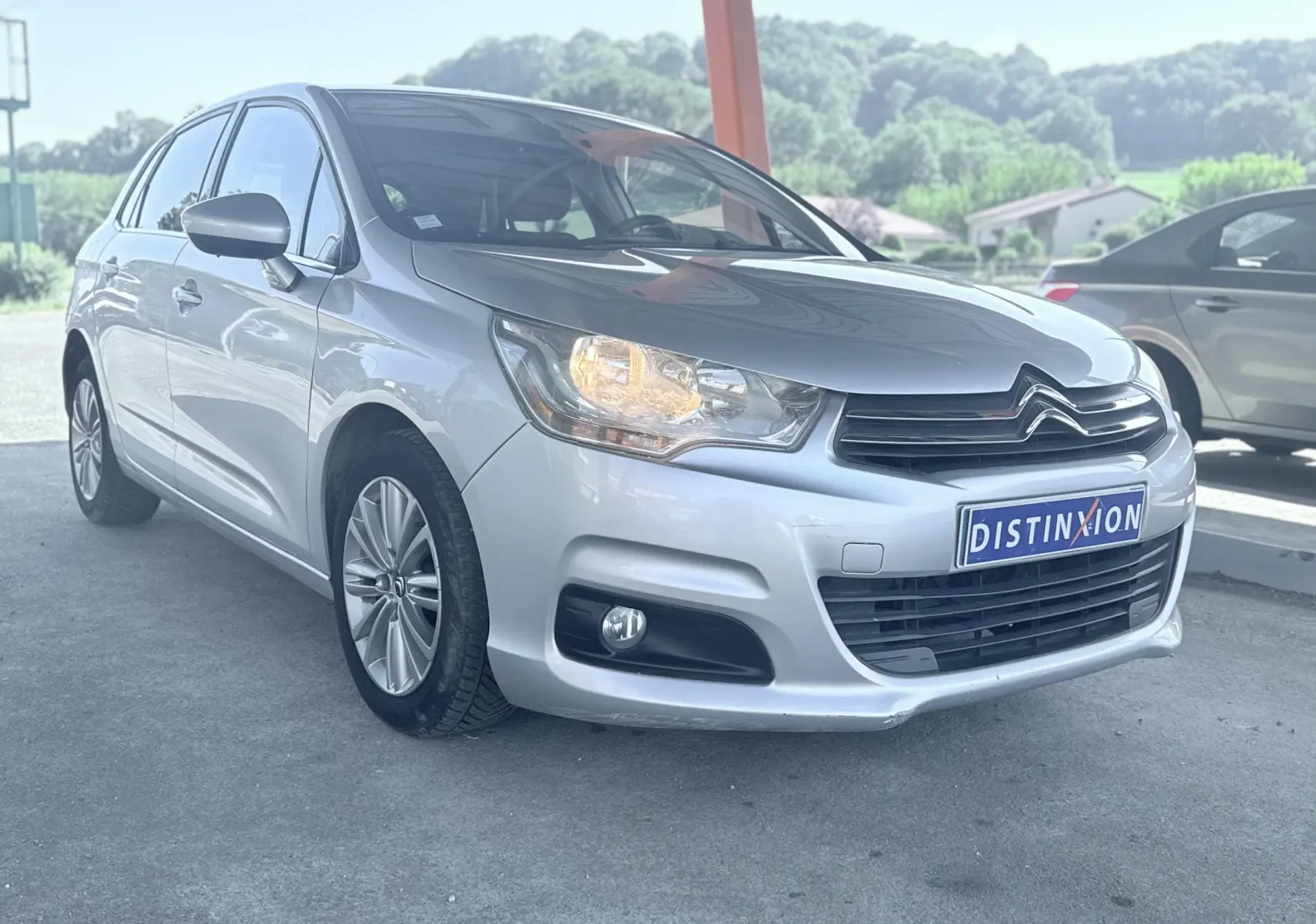 Citroën C4 gris vue 3/4 avant droit avec phare allumé, calandre noire et jantes alliage.
