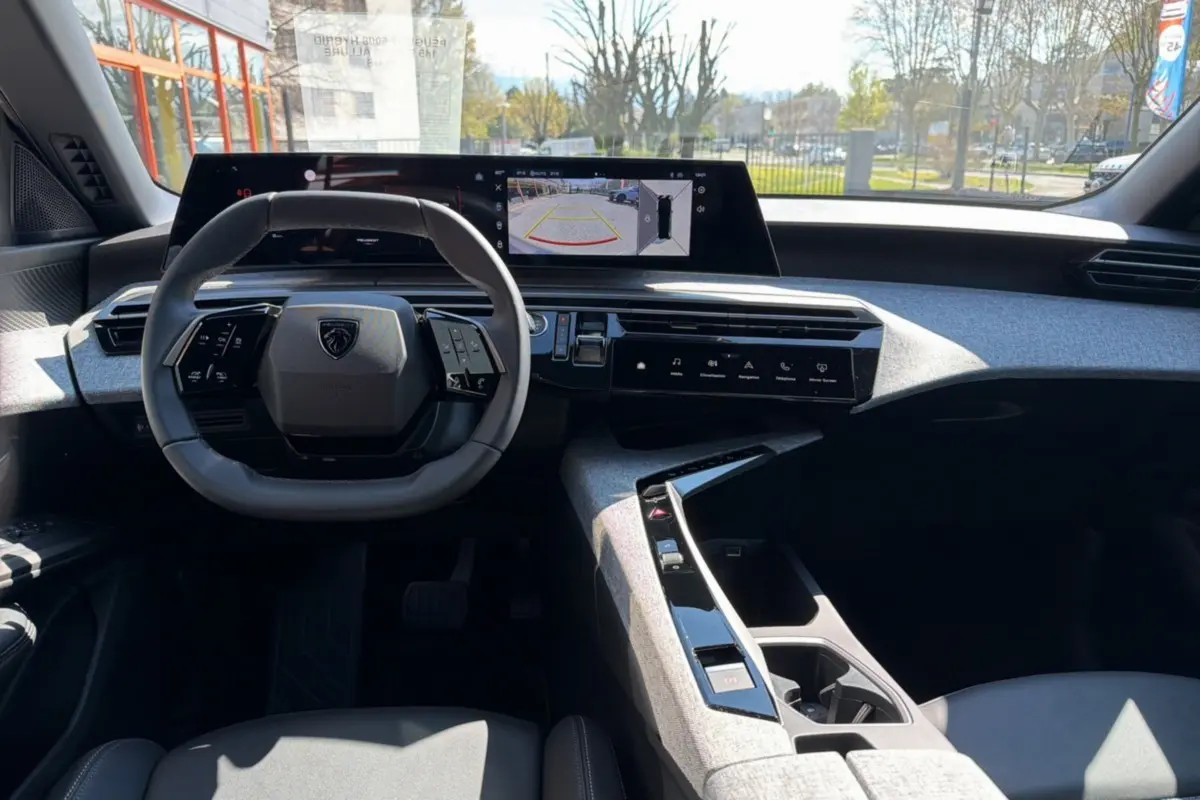 Vue intérieure avant du Peugeot 5008 Hybrid 145 Allure Plus, volant cuir multifonctions et écran panoramique 21 pouces affichant caméra 360°