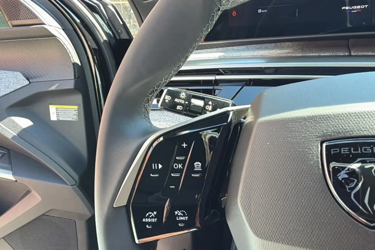 Gros plan sur le volant cuir multifonctions de la Peugeot 5008 noir perla nera, avec commandes d'assistance et régulateur.