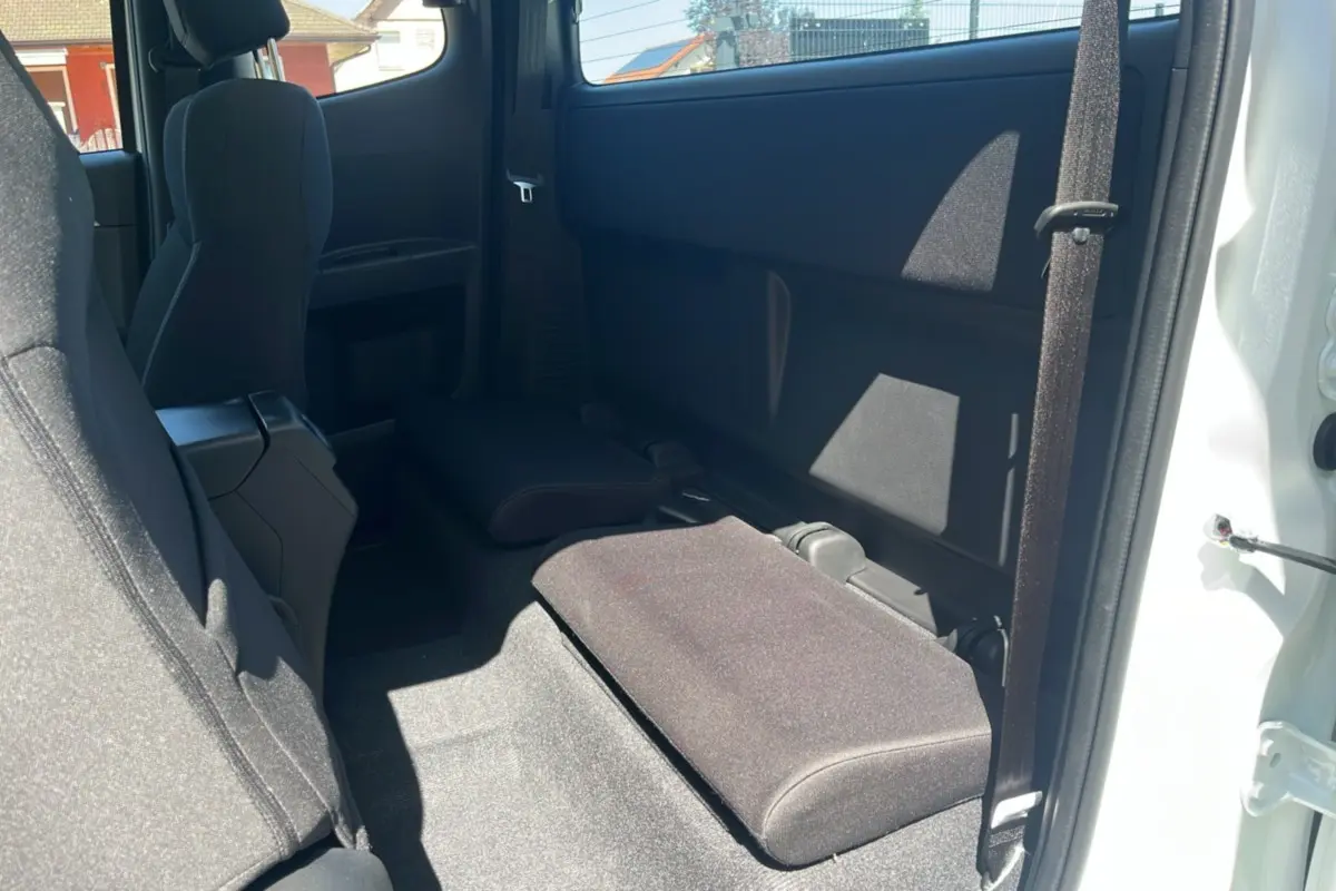 Vue intérieure arrière droite du pick-up Isuzu D-MAX 2026 blanc, montrant les strapontins rabattus en tissu noir.