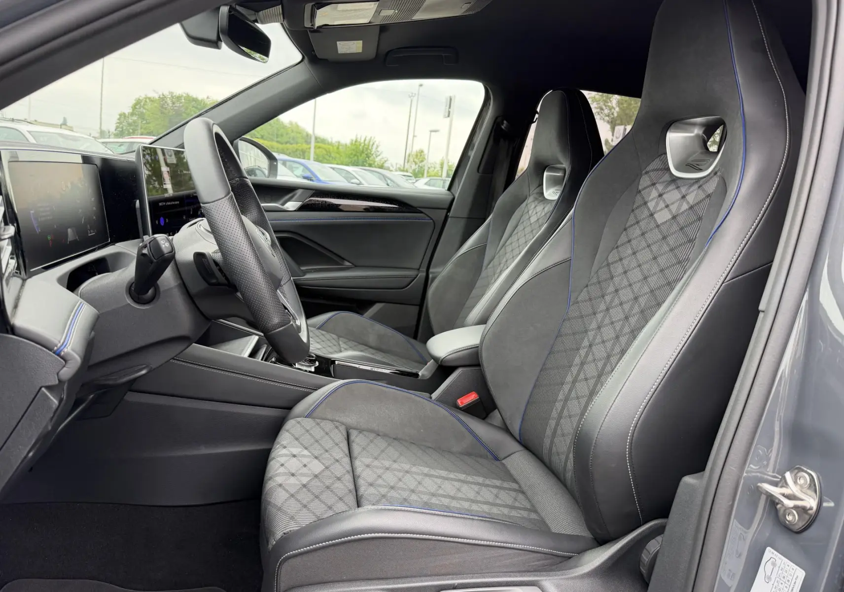 Intérieur côté conducteur du Volkswagen Tiguan gris 2025, sièges sport avec surpiqûres bleues et tableau de bord digital.
