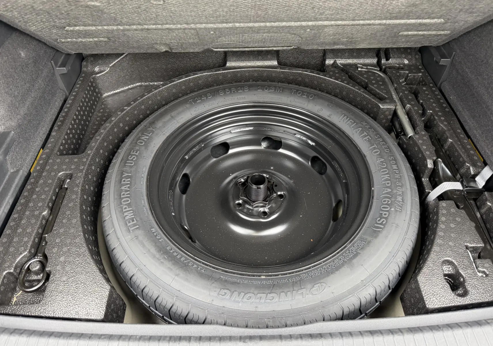 Gros plan sur la roue de secours compacte noire dans le coffre du Volkswagen Tiguan gris 2025.
