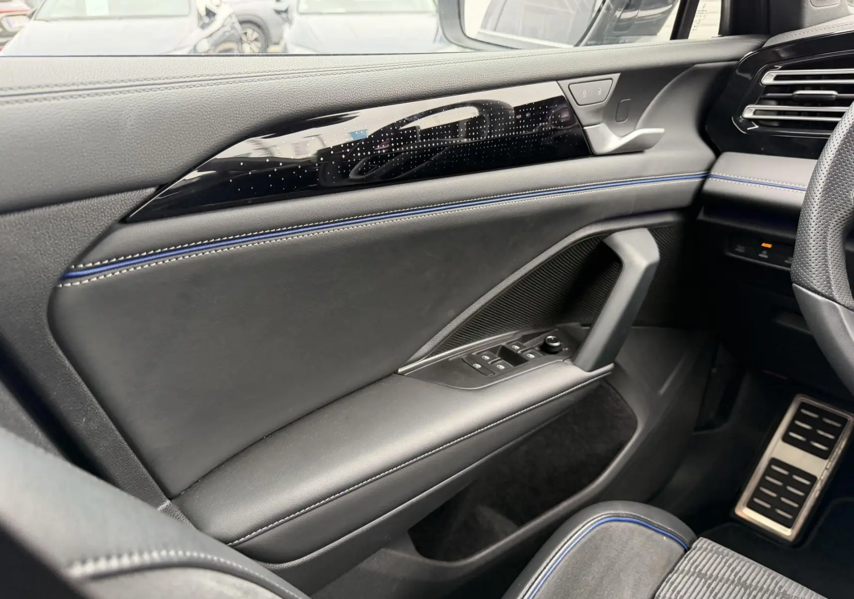 Vue intérieure côté gauche du Volkswagen Tiguan 2025, avec garniture cuir noire et surpiqûres bleues sur la porte.