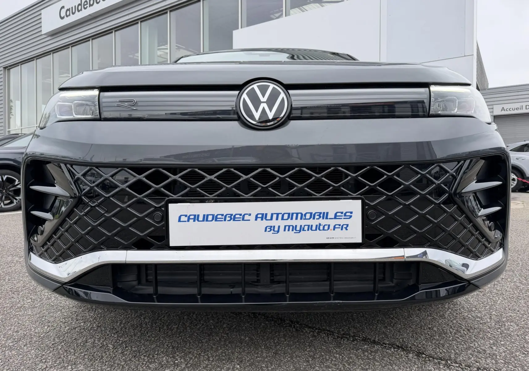 Vue frontale rapprochée du Volkswagen Tiguan gris 2025 avec calandre noire à motif losange et logo VW central lumineux.