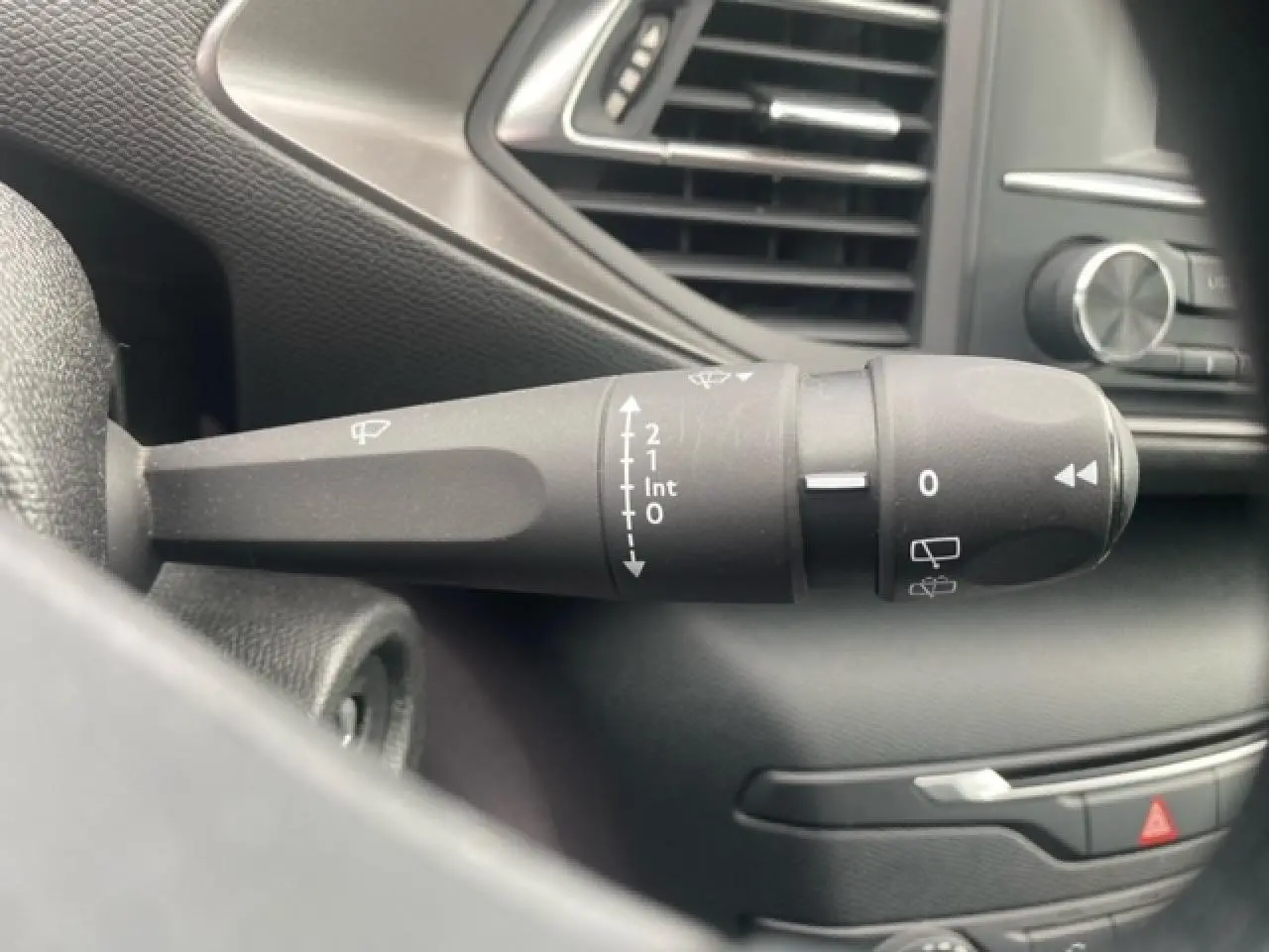 Gros plan sur la commande d'essuie-glace noire à gauche du volant dans l'habitacle d'une Peugeot 308 SW gris clair.