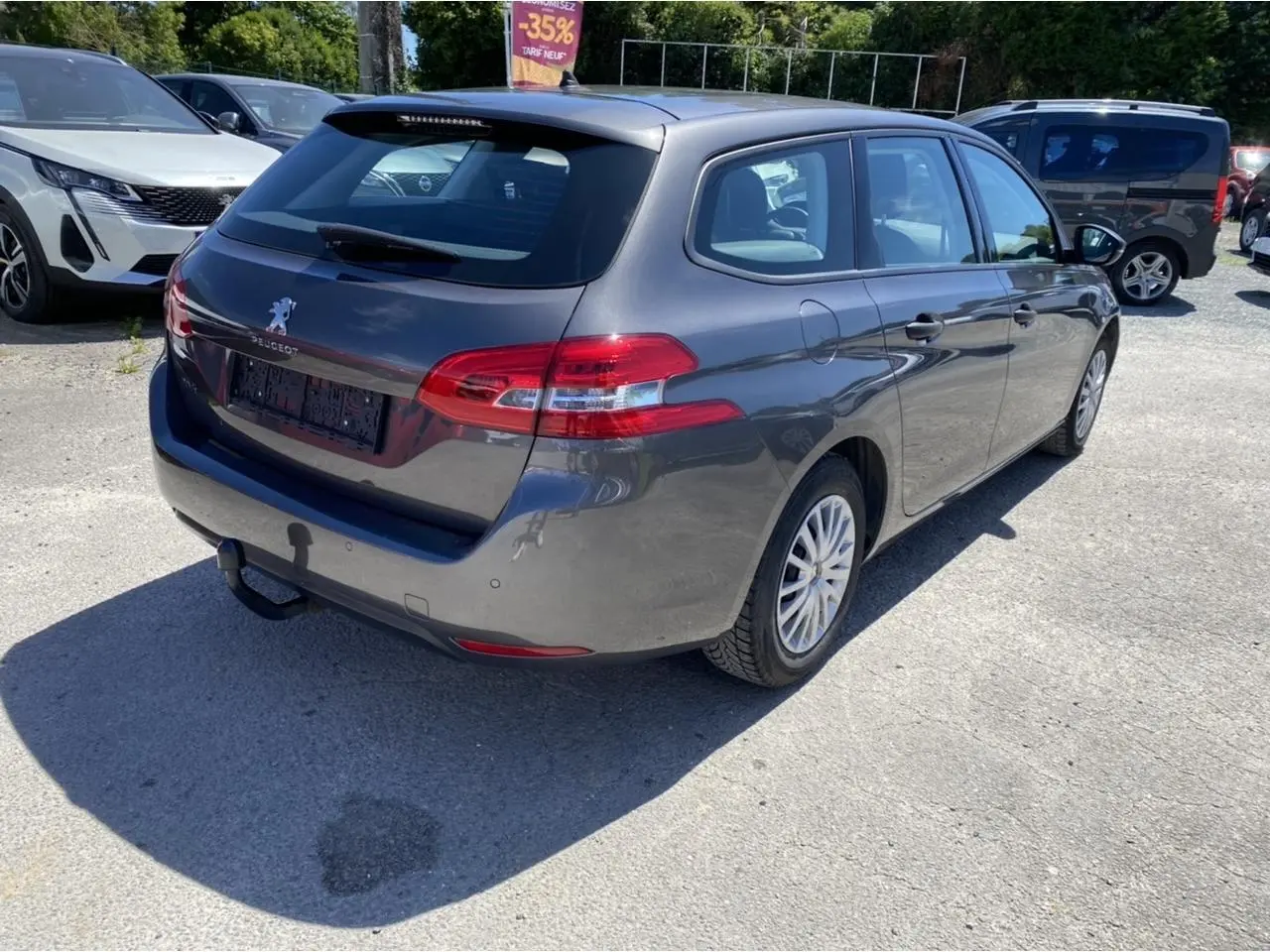 Peugeot 308 SW gris clair vue 3/4 arrière droit avec attelage de remorque sur un parking ensoleillé.