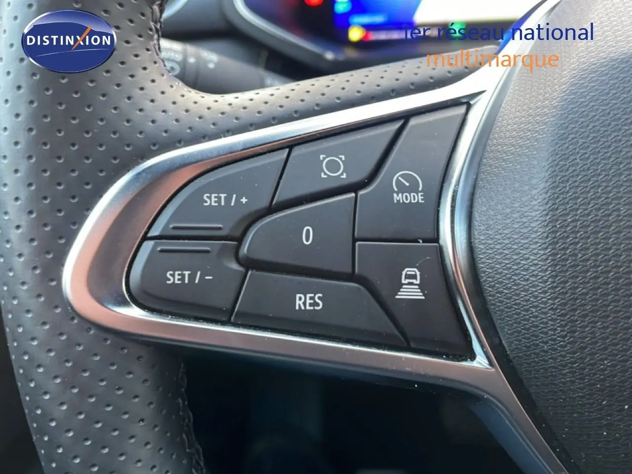 Gros plan sur les commandes au volant en cuir perforé du Renault Symbioz gris Cassiopée, avec boutons de régulateur et mode.