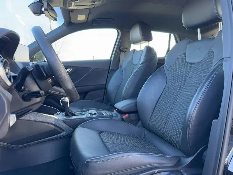 Vue intérieure côté conducteur de l'Audi Q2 30 TDI 2024 avec sièges sport noirs en cuir et volant multifonction.