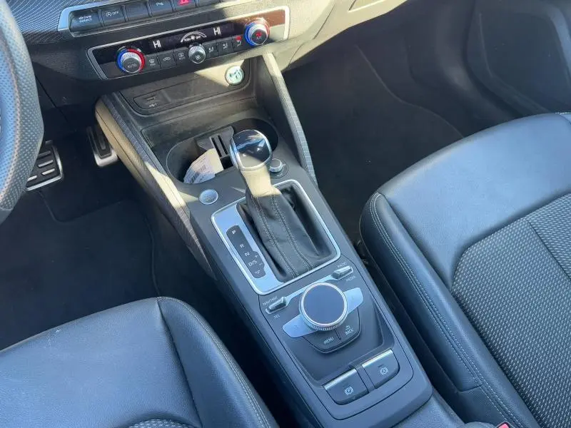 Vue intérieure centrée sur la console centrale et levier de vitesse de l'Audi Q2 30 TDI noir Mythic, sièges en cuir noir.