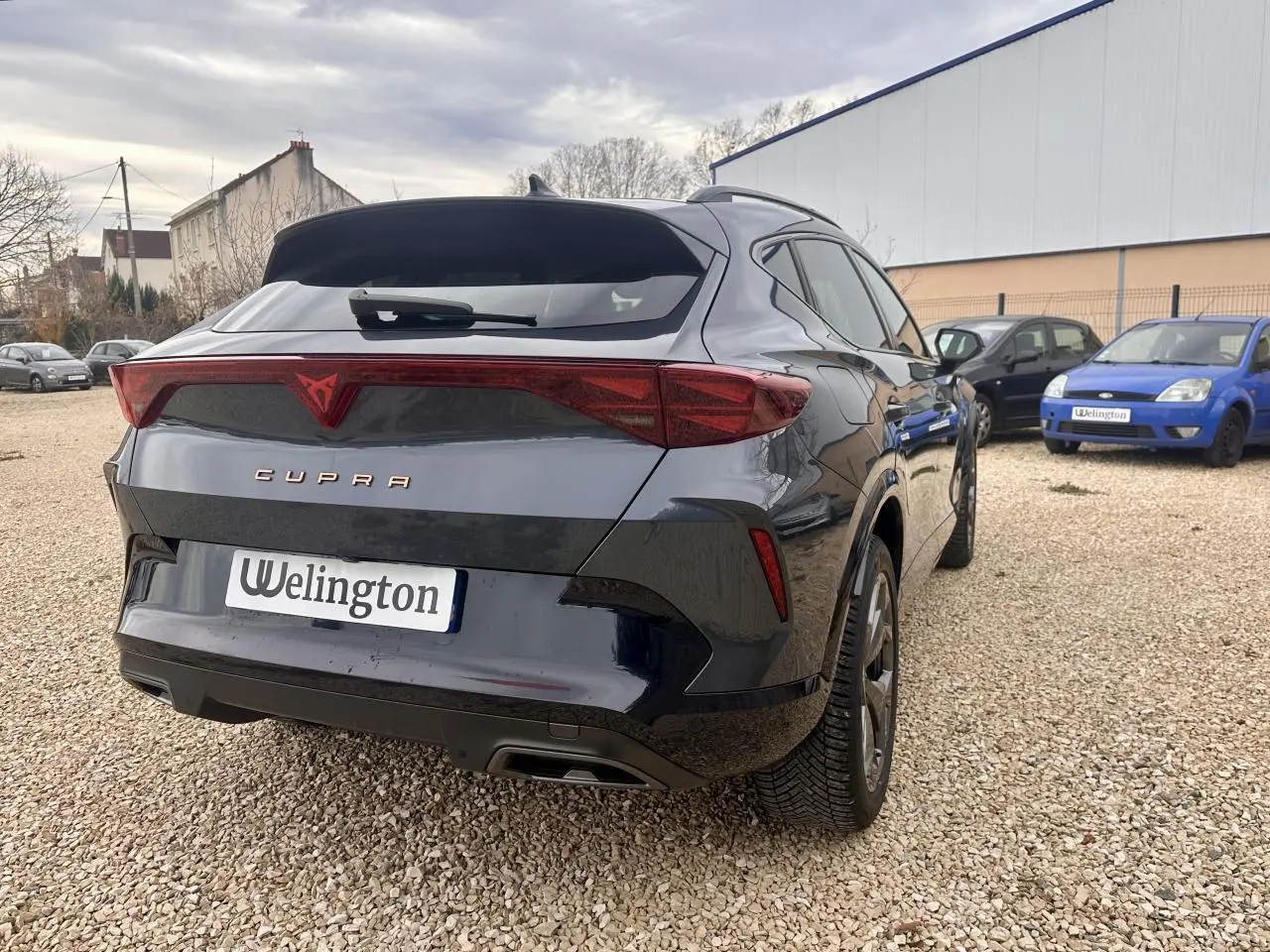 Vue 3/4 arrière droite d'une CUPRA Formentor gris foncé avec feux arrière triangulaires et logo rouge distinctif.