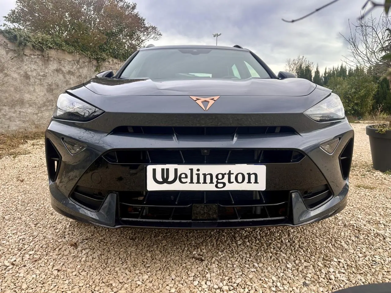 Vue avant d'une CUPRA Formentor gris foncé avec logo cuivre et calandre large sur un sol gravillonné.