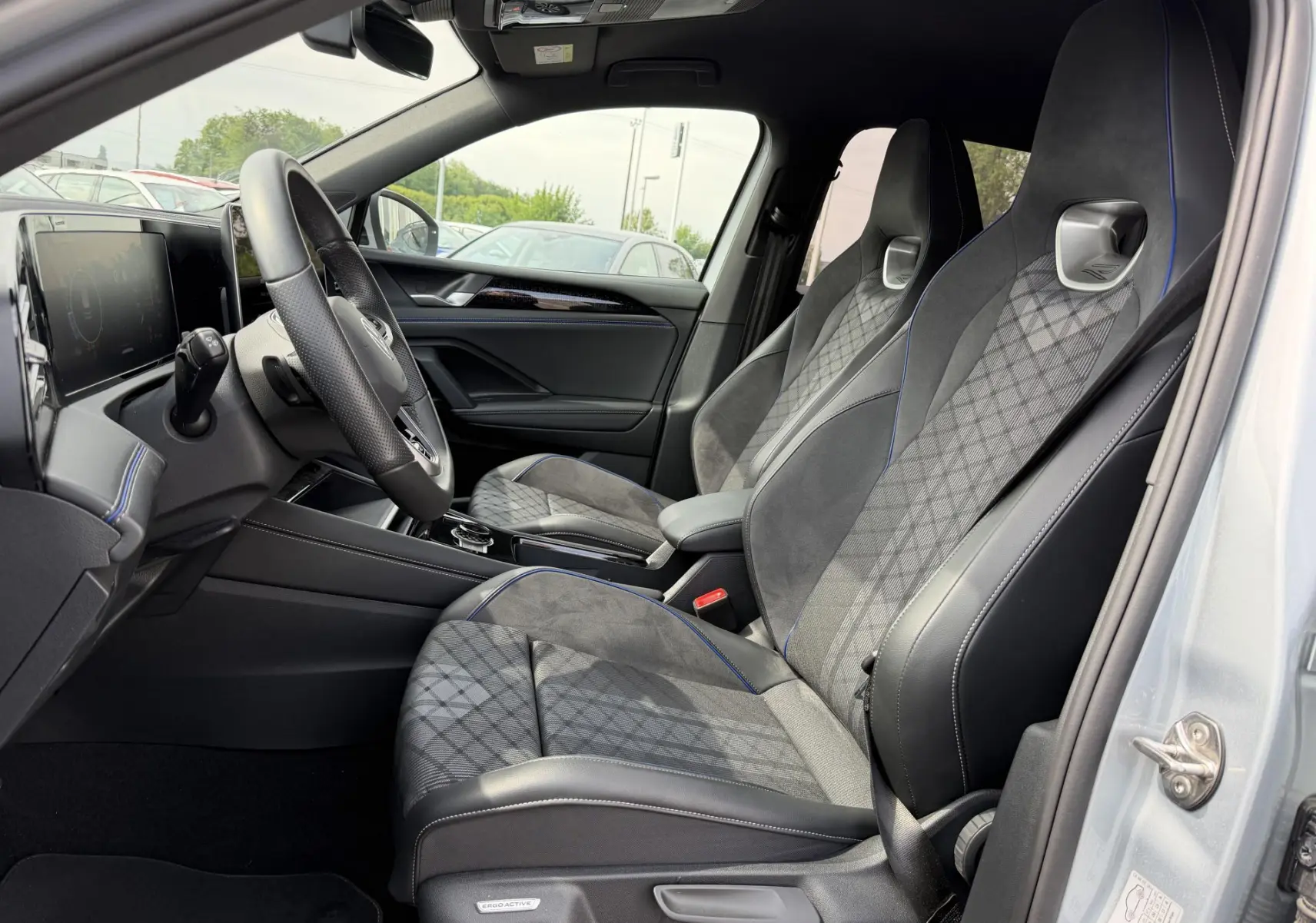 Vue intérieure côté conducteur du Volkswagen Tiguan 2025 avec sièges sport gris à surpiqûres bleues et volant multifonction cuir.