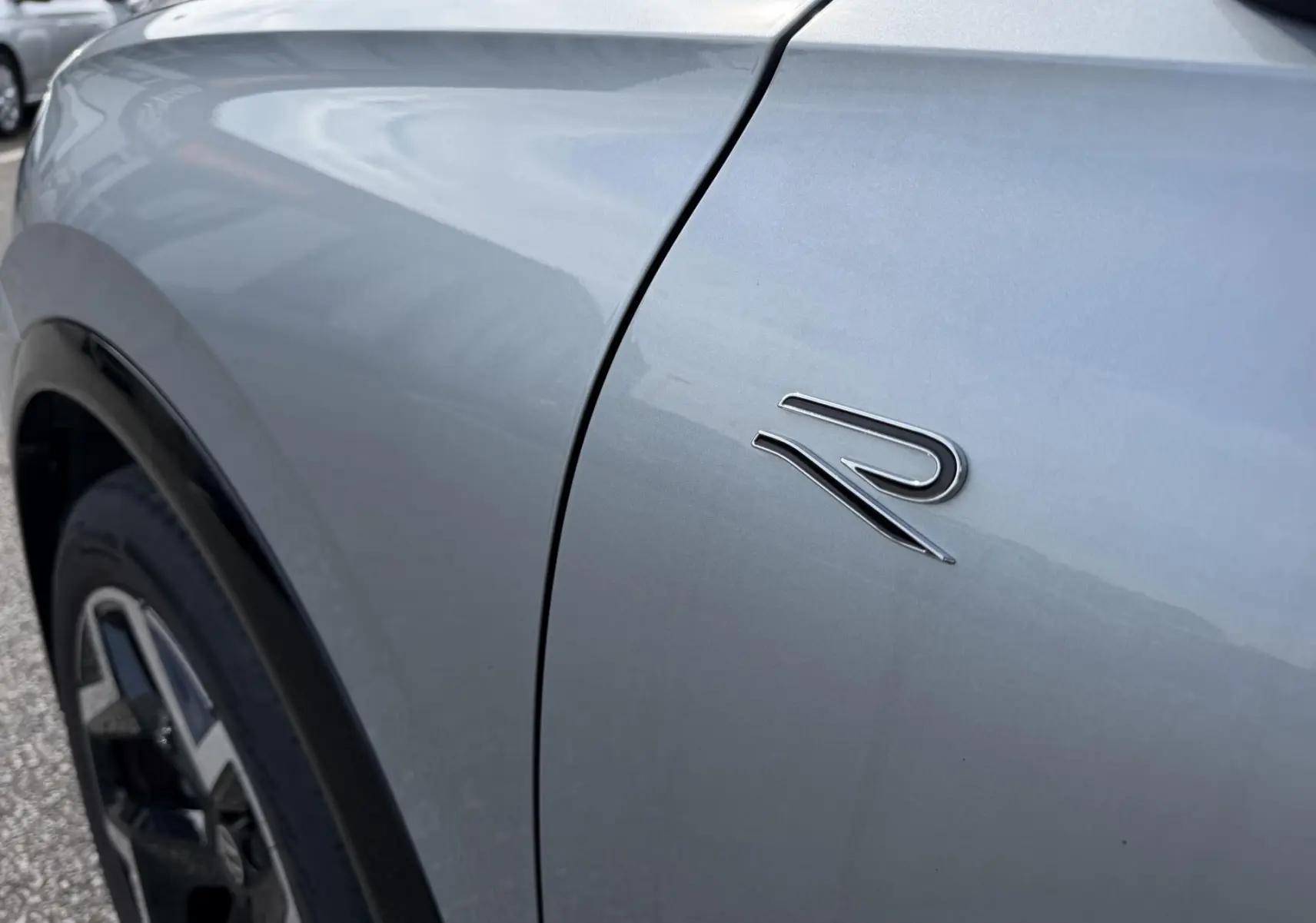 Détail du logo R sur l'aile avant gauche d'un Volkswagen Tiguan gris métallisé, avec jante noire visible.