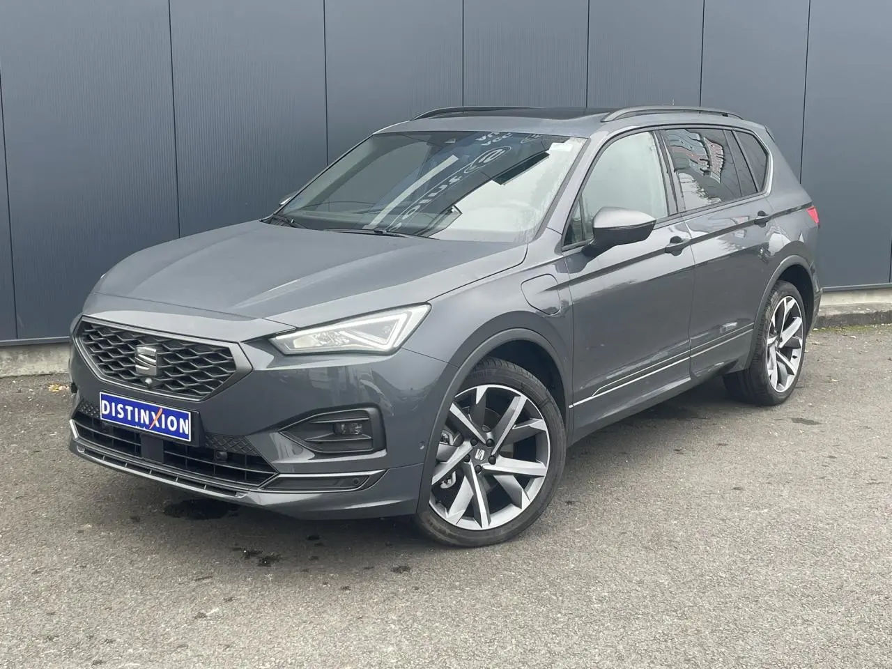 SEAT Tarraco gris dauphin en 3/4 avant droit, toit ouvrant panoramique et jantes alliage 20 pouces visibles.