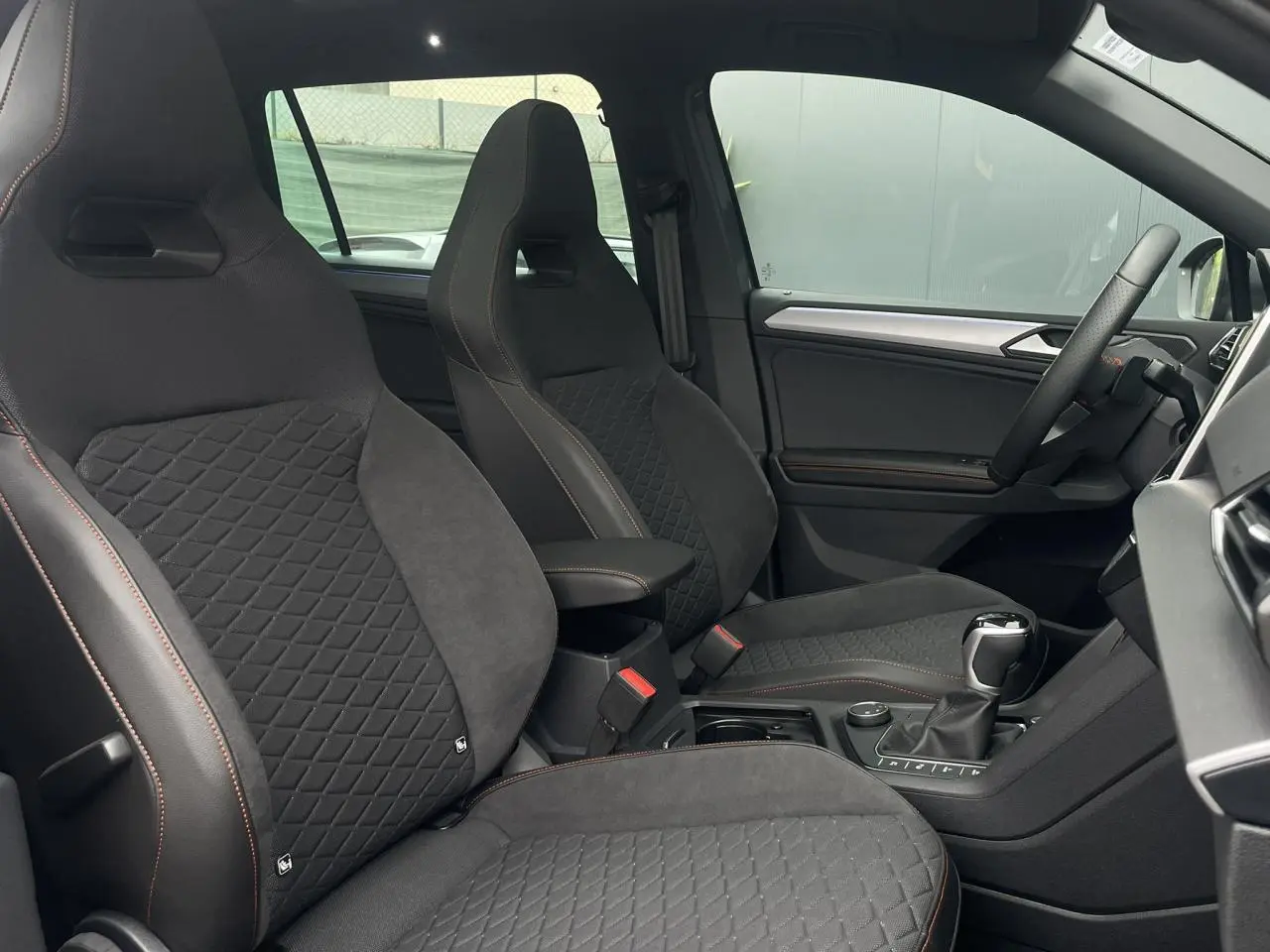 Intérieur du SEAT Tarraco 1.4 e-Hybrid 2024, vue côté conducteur, sièges sport noirs avec surpiqûres orange.