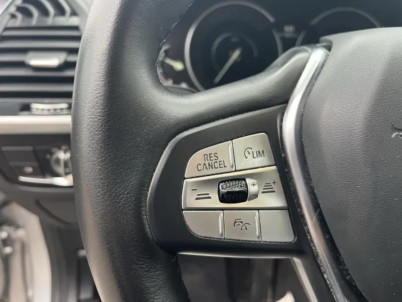 Gros plan sur les commandes de régulateur de vitesse au volant cuir noir d'une BMW X3 xDrive30eA 2020.