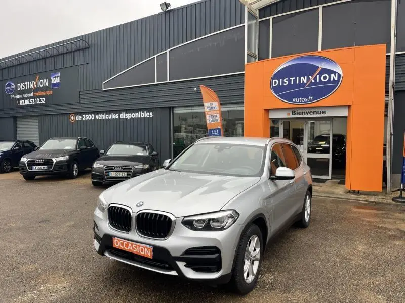 BMW X3 xDrive30e glaciersilber en 3/4 avant droit, stationné devant un concessionnaire Distinxion.