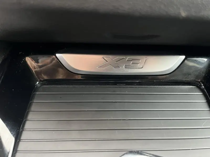 Gros plan sur la plaque X3 en métal brossé dans l'habitacle noir d'une BMW X3 xDrive30e 2020.
