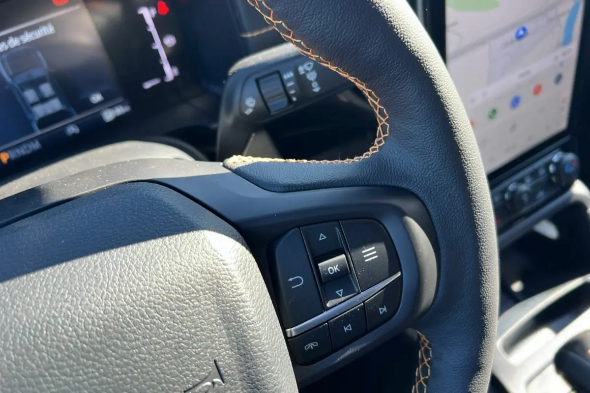 Gros plan sur le volant avec commandes intégrées du Ford Ranger 2025 bleu lightning, tableau de bord et écran tactile en arrière-plan.