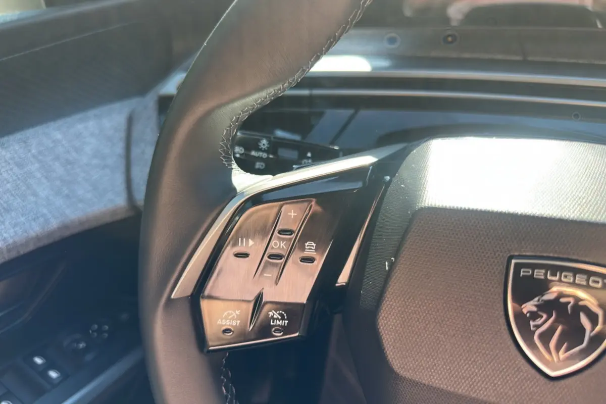 Gros plan sur le volant cuir noir du Peugeot 5008 Hybrid 145, avec commandes multifonctions et logo lion central.