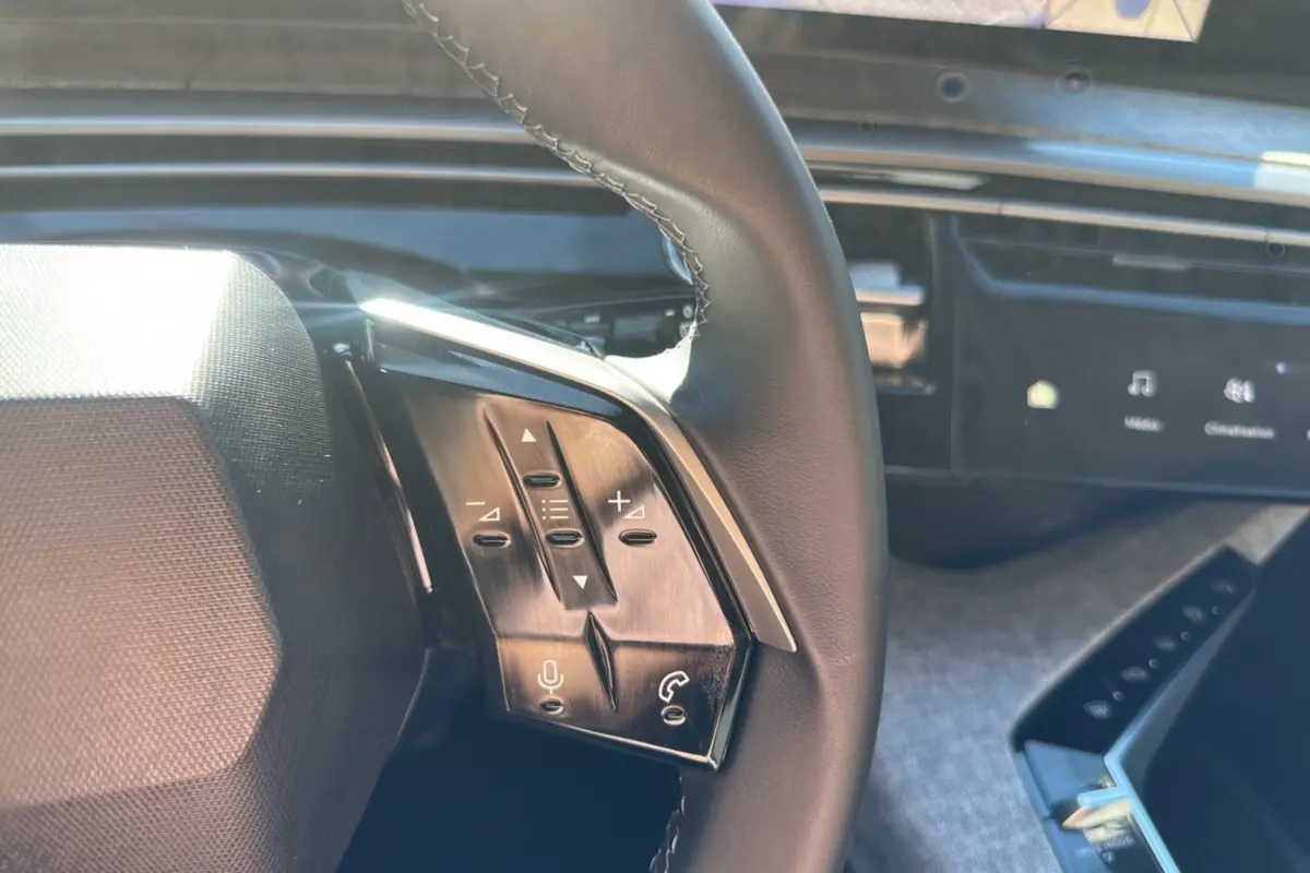 Gros plan sur le volant cuir multifonctions de la Peugeot 5008 gris artense, avec commandes vocales et audio visibles.