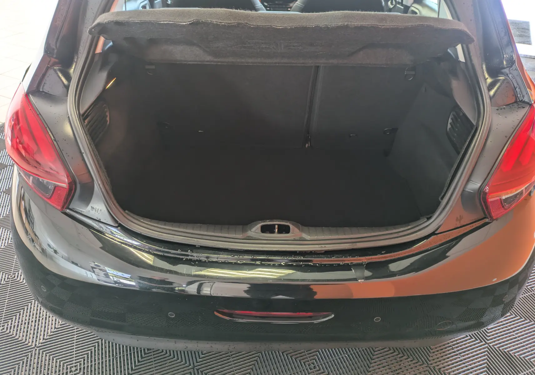 Coffre ouvert vu de l'arrière d'une Peugeot 208 Allure noire, montrant l'espace de chargement vide et la plage arrière relevée.