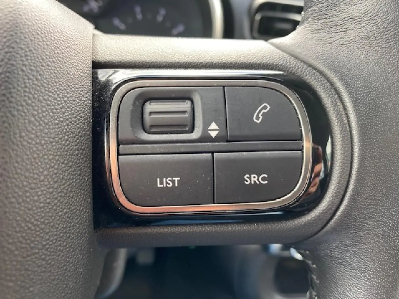 Gros plan sur les commandes au volant du Citroën C3 gris clair 2017, boutons pour téléphone et liste audio.