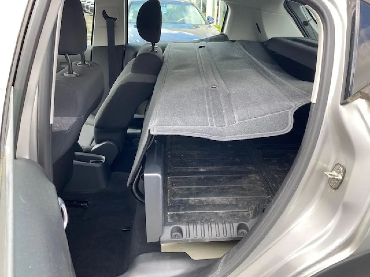 Vue intérieure côté droit d'une Citroën C3 gris clair 2017 avec siège arrière rabattue et tapis de coffre visible.