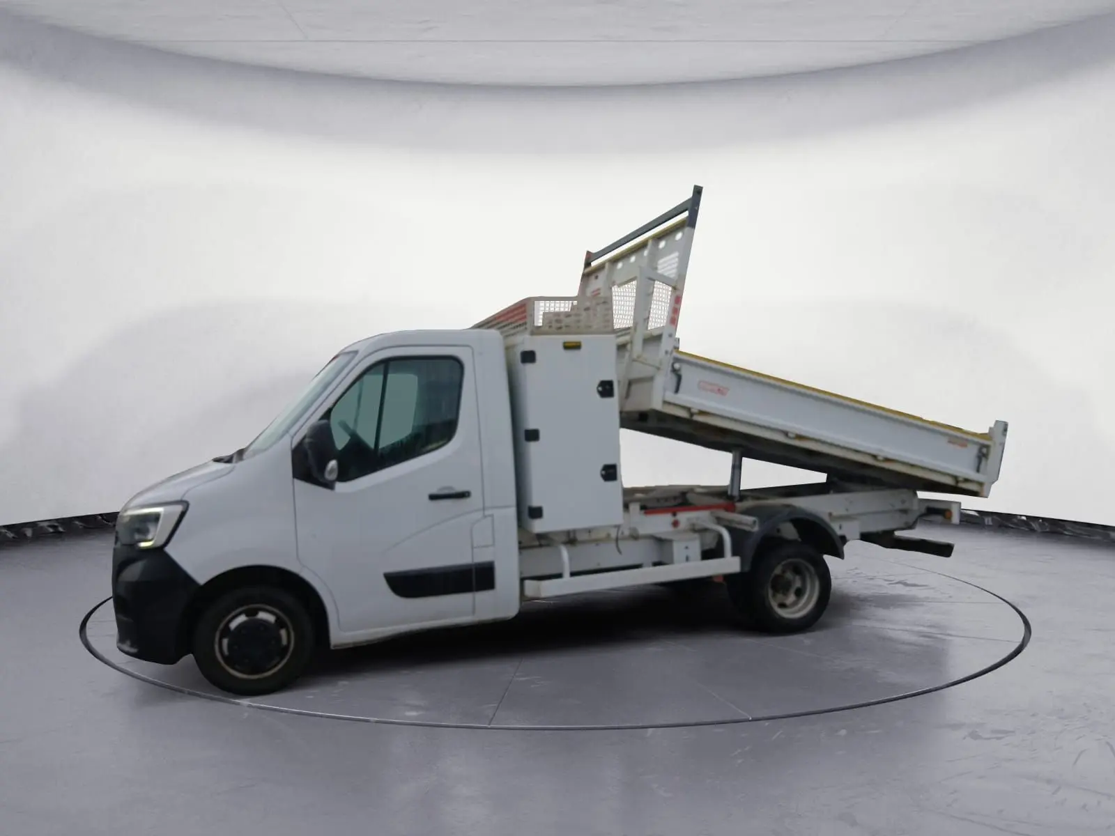 Renault Master blanc vu de profil gauche avec benne basculante relevée et coffre latéral fermé.
