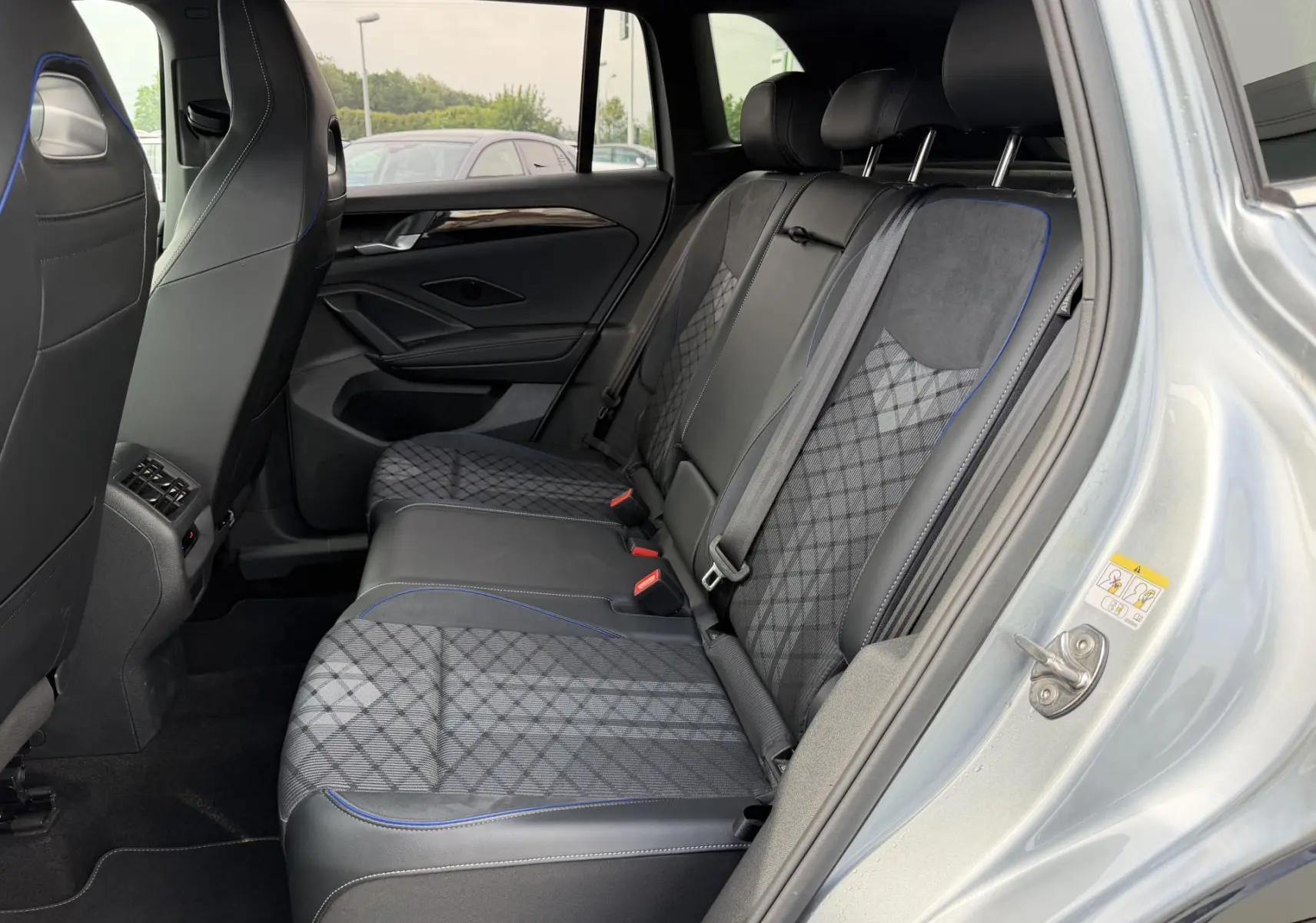 Vue latérale intérieure côté droit du Volkswagen Tiguan 2025 gris, montrant les sièges arrière en tissu et cuir avec surpiqûres bleues.