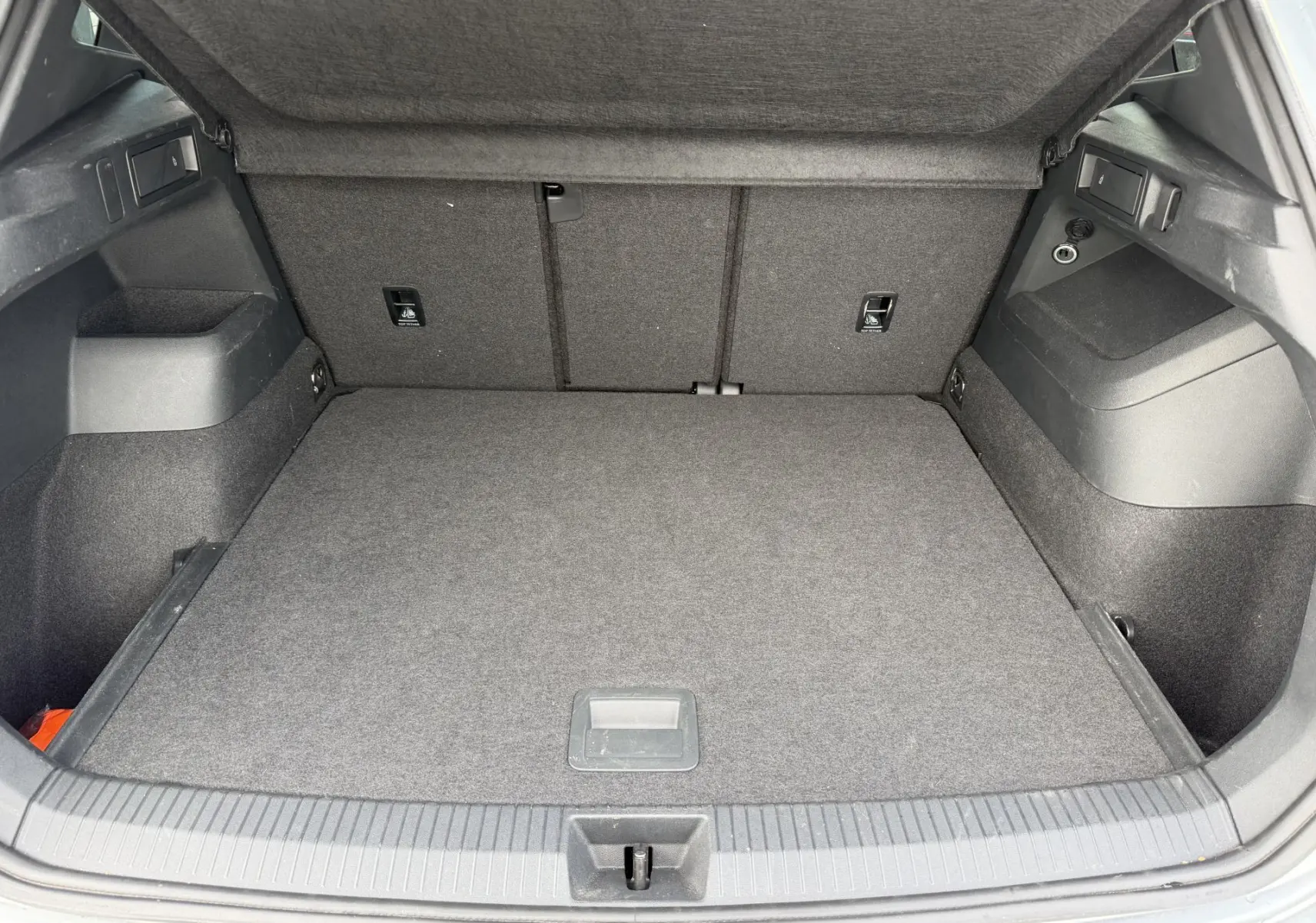 Coffre ouvert du Volkswagen Tiguan gris, vue arrière montrant l'espace de chargement et les rangements latéraux.
