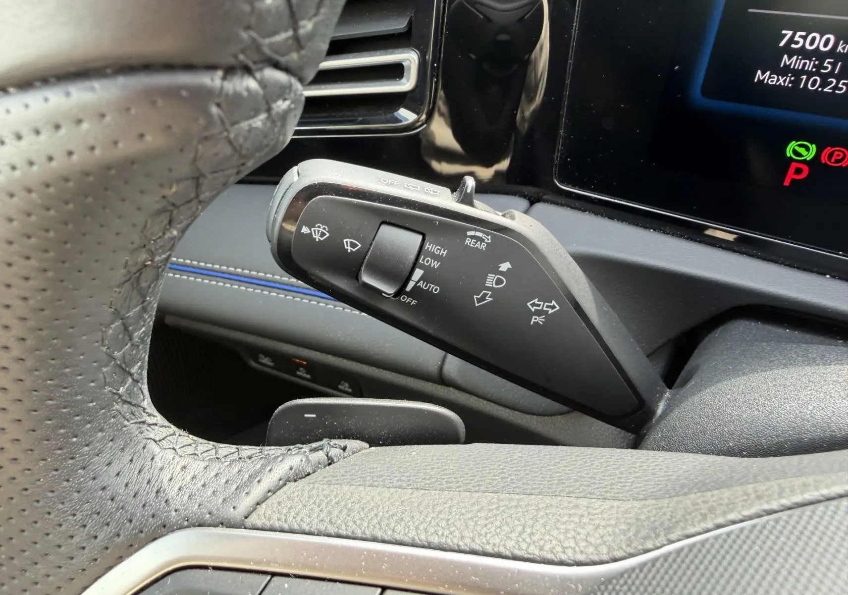 Gros plan sur la manette de commandes des essuie-glaces et clignotants du Volkswagen Tiguan 2025, intérieur noir avec surpiqûres bleues.