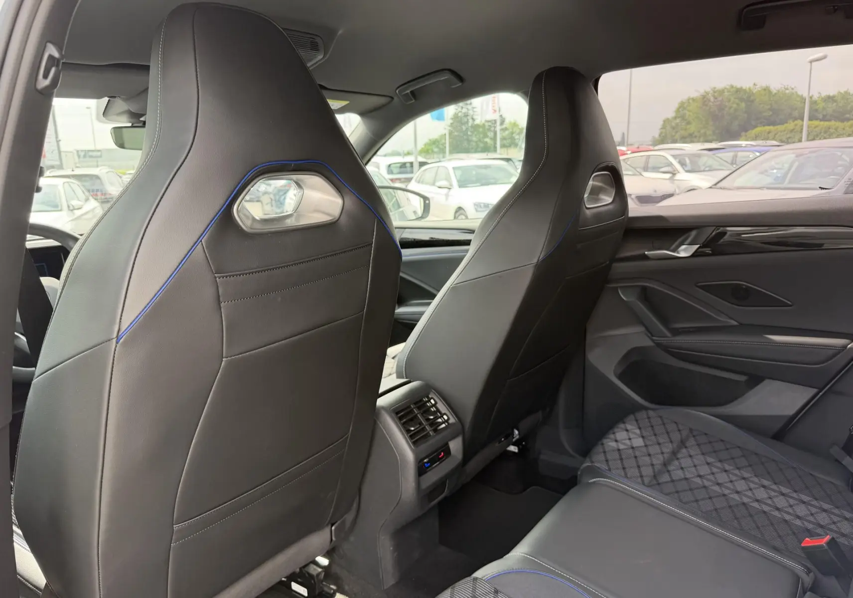 Vue intérieure arrière du Volkswagen Tiguan 2025, sièges avant sport noirs avec surpiqûres bleues et aérateurs centraux.