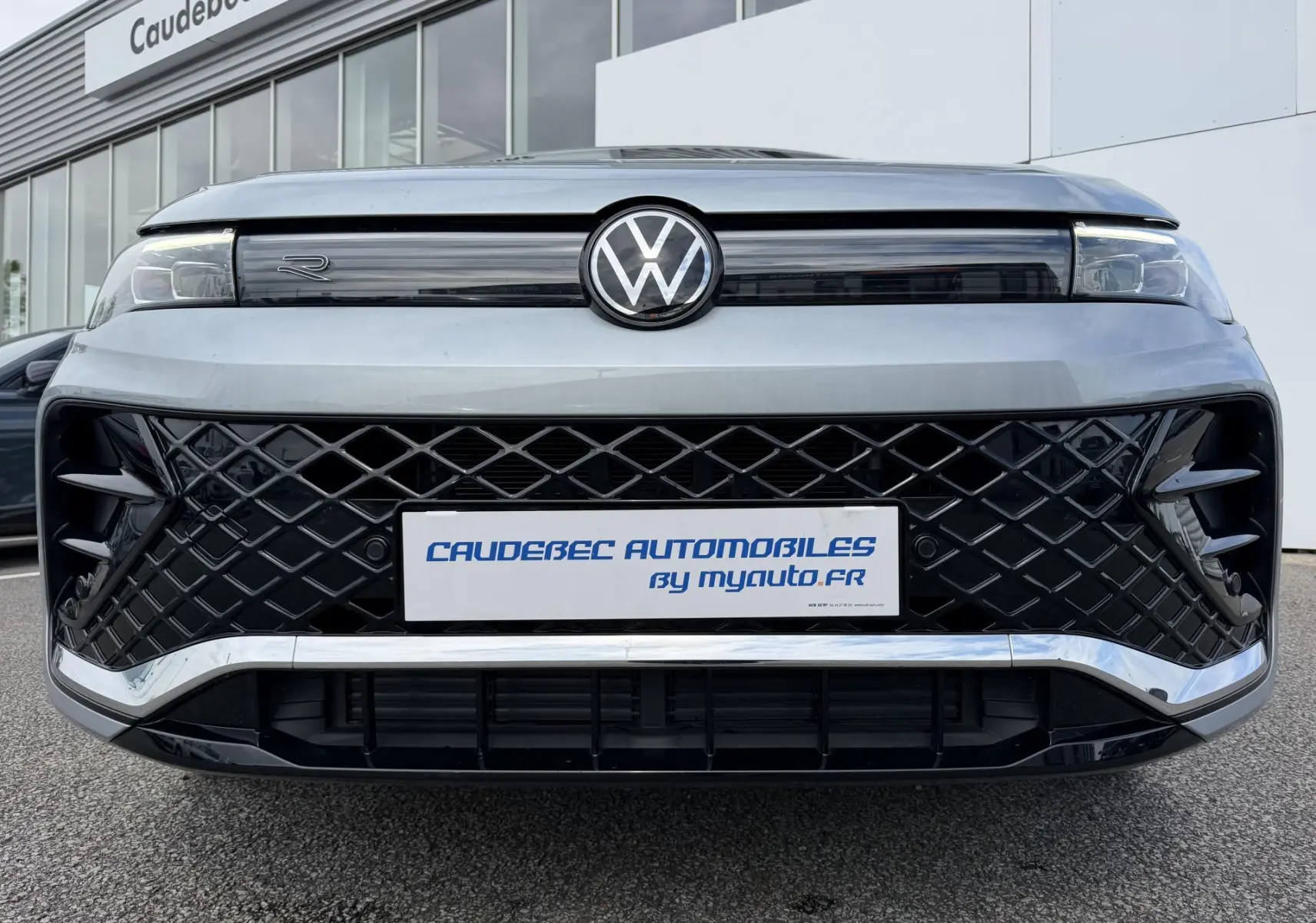 Vue frontale du Volkswagen Tiguan gris avec calandre noire à motif losange et logo VW central lumineux.