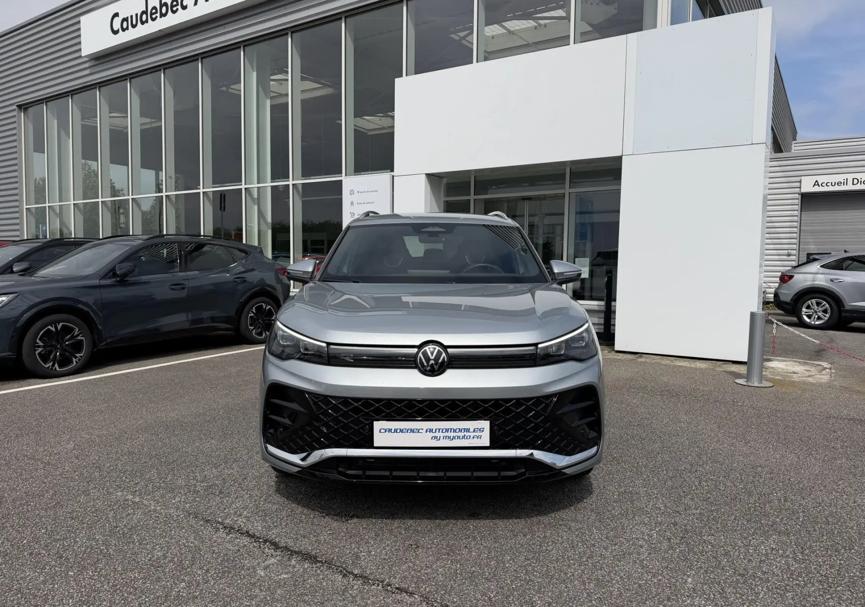 Volkswagen Tiguan gris vue de face, avec calandre noire et phares LED, devant un showroom automobile.