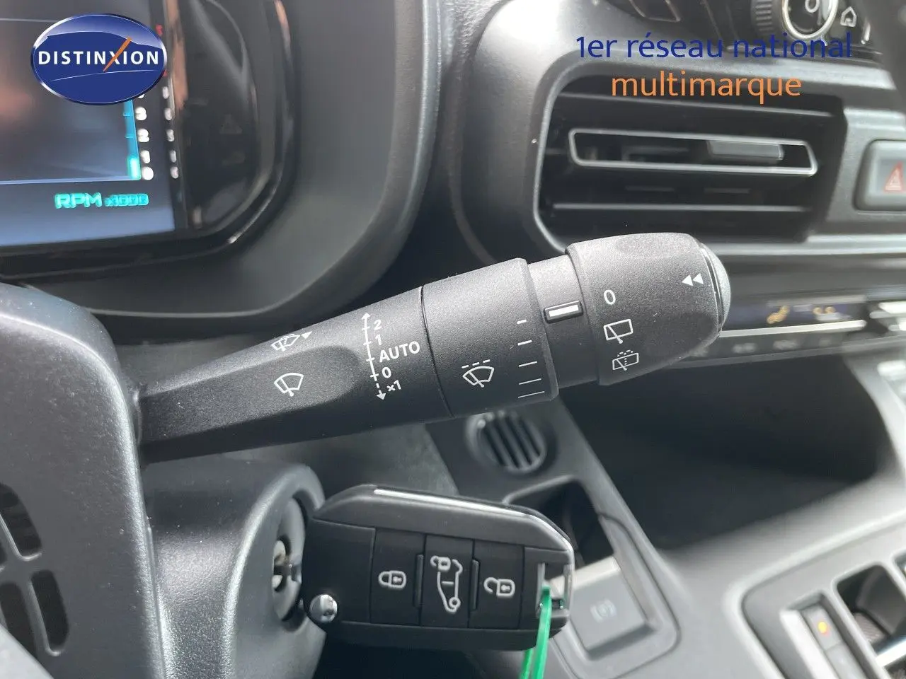 Gros plan sur la commande d’essuie-glace et la clé insérée dans le contacteur d’un Citroën Berlingo noir, intérieur tableau de bord.