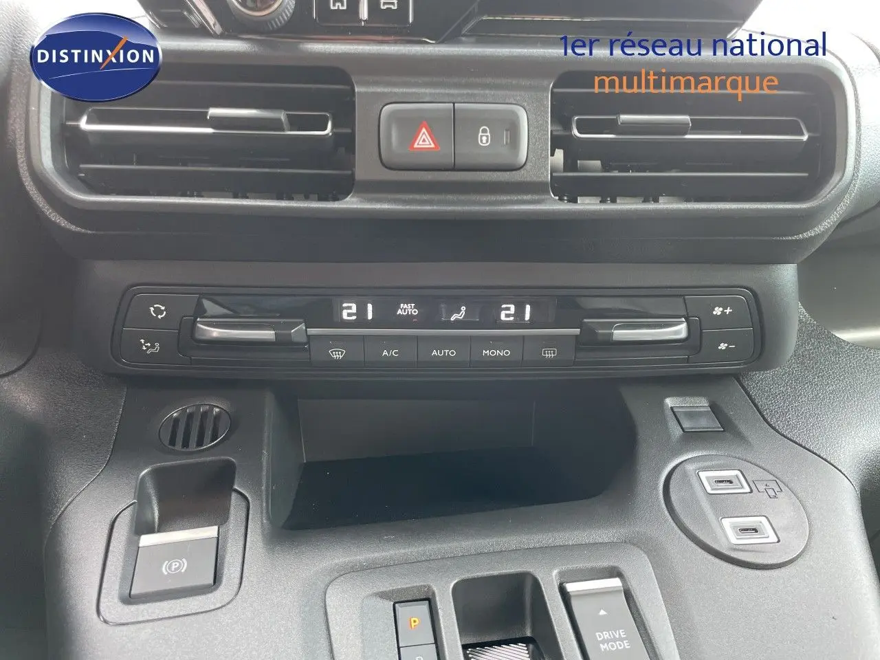 Vue rapprochée de la console centrale du Citroën Berlingo noir, montrant les commandes de climatisation et le frein à main électrique.
