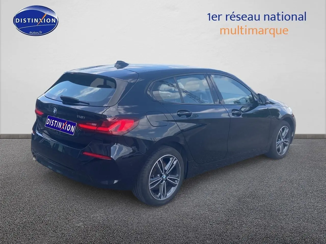 BMW Série 1 noire vue en 3/4 arrière côté droit, avec jantes alliage et feux arrière LED allumés.