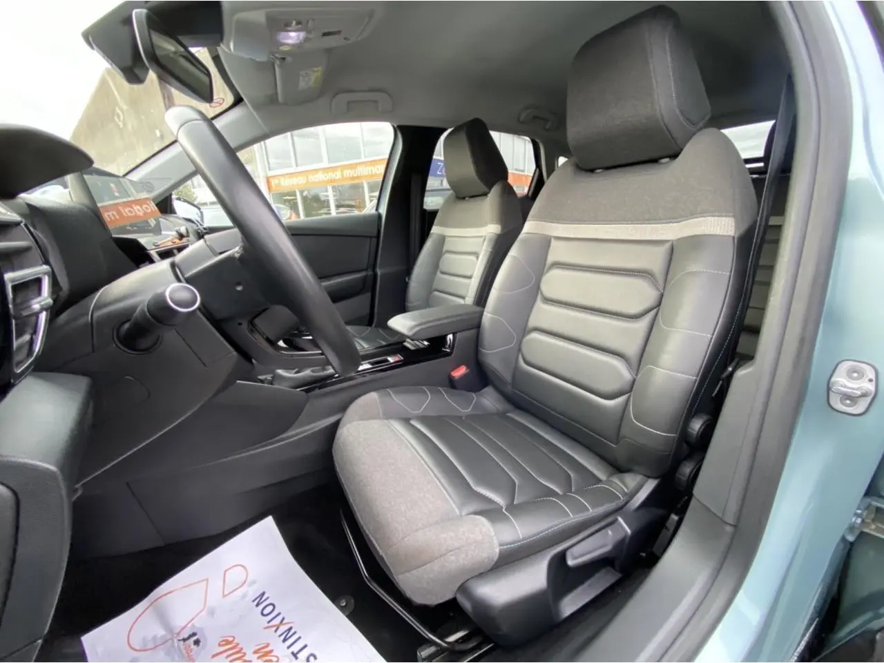 Vue intérieure côté conducteur de la Citroën C4 2021 bleu Iceland, sièges bi-matière gris et noir avec accoudoir central.