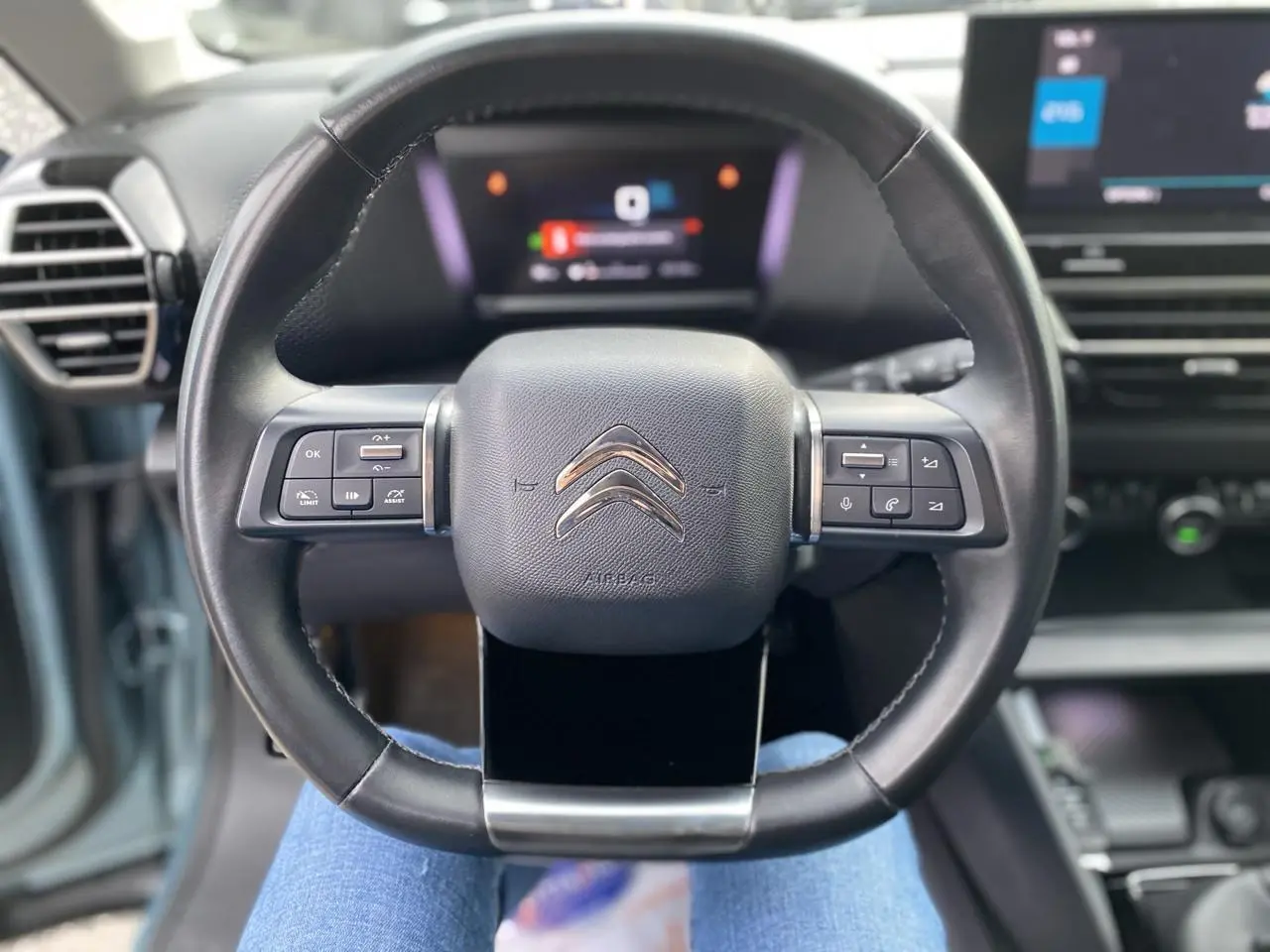 Volant cuir noir de Citroën C4 2021 vu de face, avec commandes intégrées et tableau de bord numérique flou.