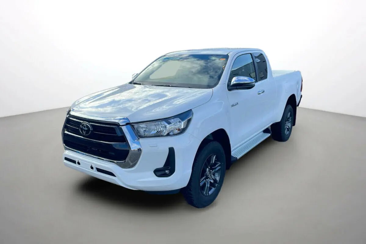 Toyota Hilux 4x4 blanc pur en 3/4 avant droit, avec calandre noire et jantes foncées visibles sur fond neutre.
