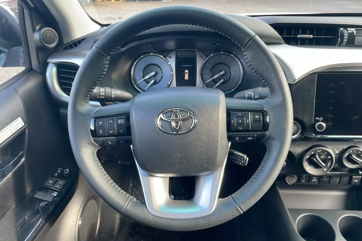 Vue intérieure centrée sur le volant cuir du Toyota Hilux 2025, avec tableau de bord et commandes visibles.