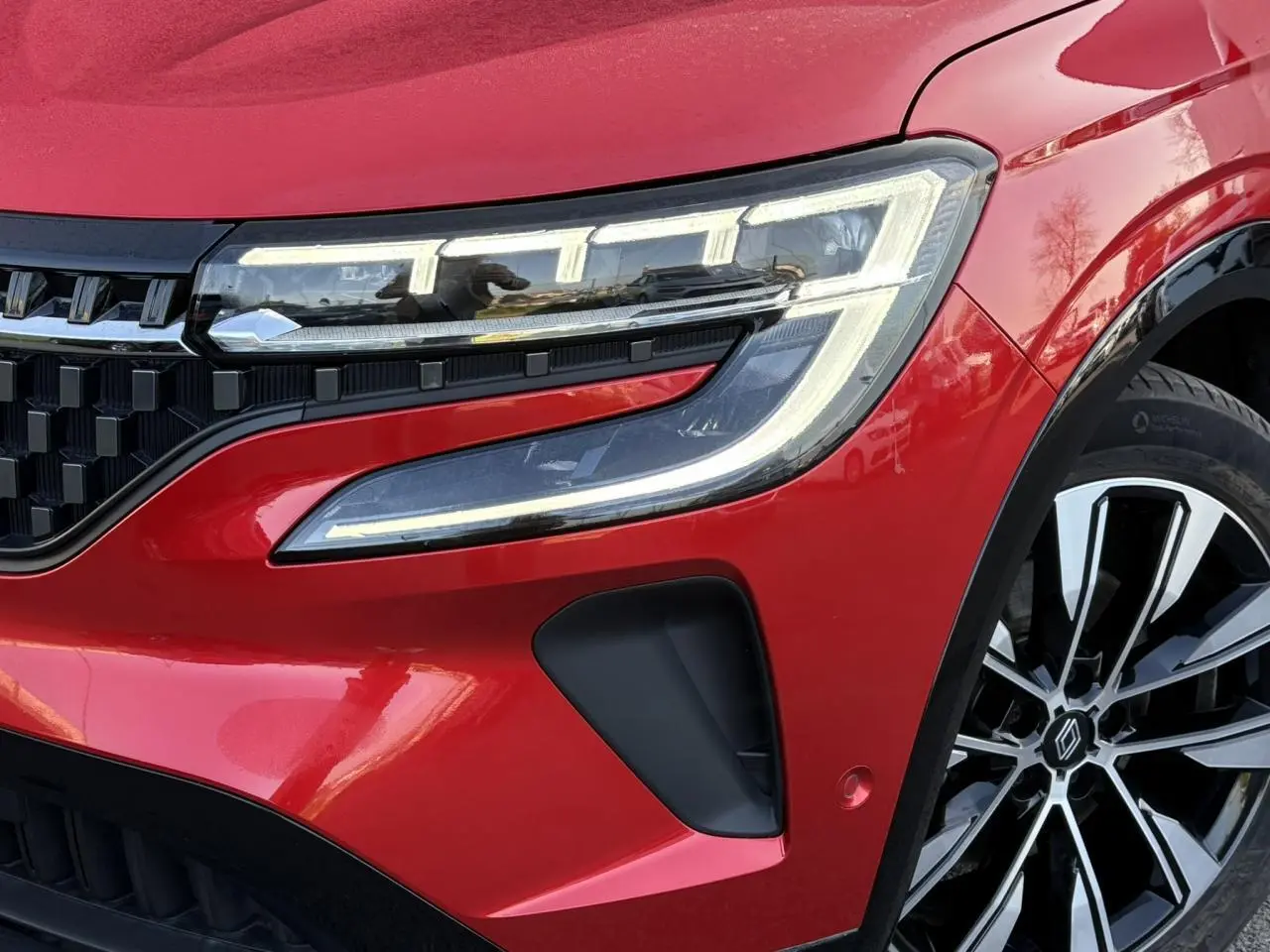 Gros plan sur le phare avant droit et la jante alliage noire et argent du Renault Austral Rouge Flamme 2024.