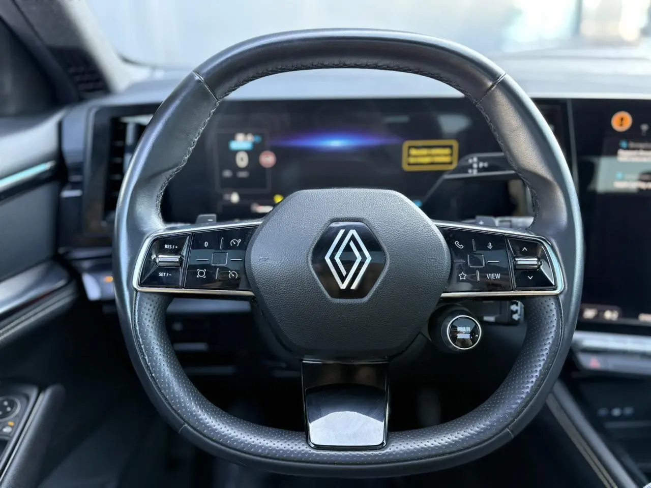 Volant cuir noir Renault avec commandes intégrées, vue frontale sur le tableau de bord numérique du Renault Austral 2024.