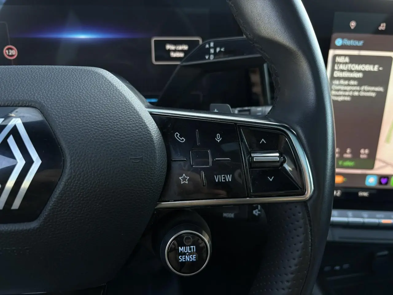 Gros plan sur le volant cuir du Renault Austral rouge, avec commandes multifonctions et bouton Multi-Sense éclairé.