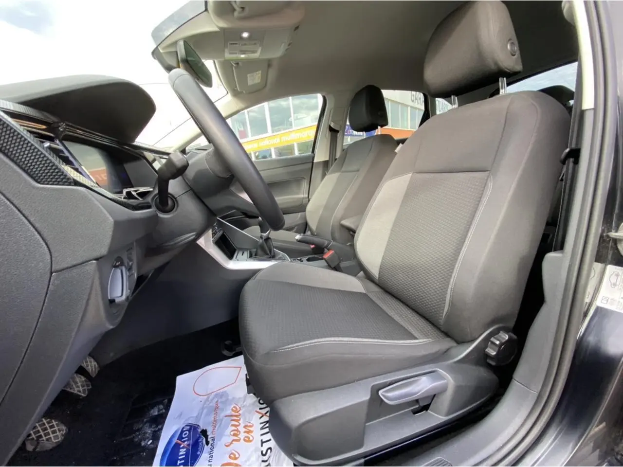 Intérieur côté conducteur du Volkswagen Taigo noir intense 2022, sièges tissu gris et console centrale visible.